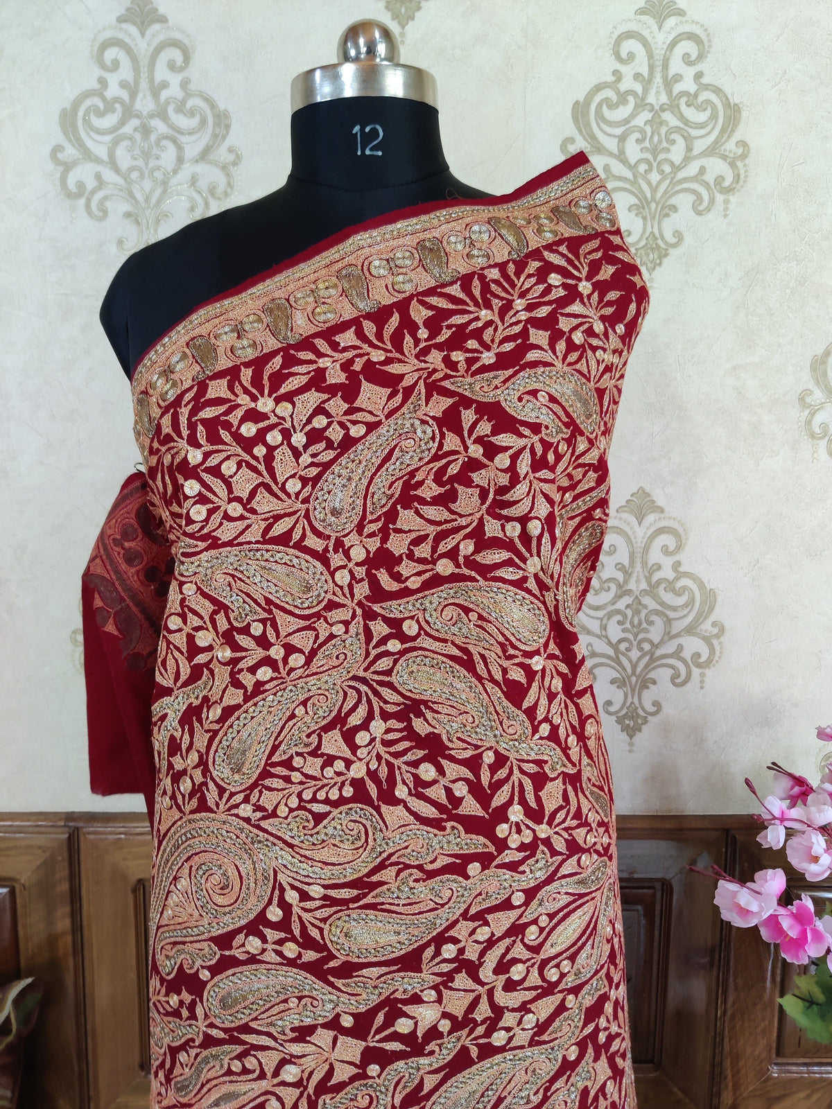 Close-up of a maroon Merino wool shawl draped across a mannequin's shoulder, with pale metallic Tilla paisleys and curled leaves