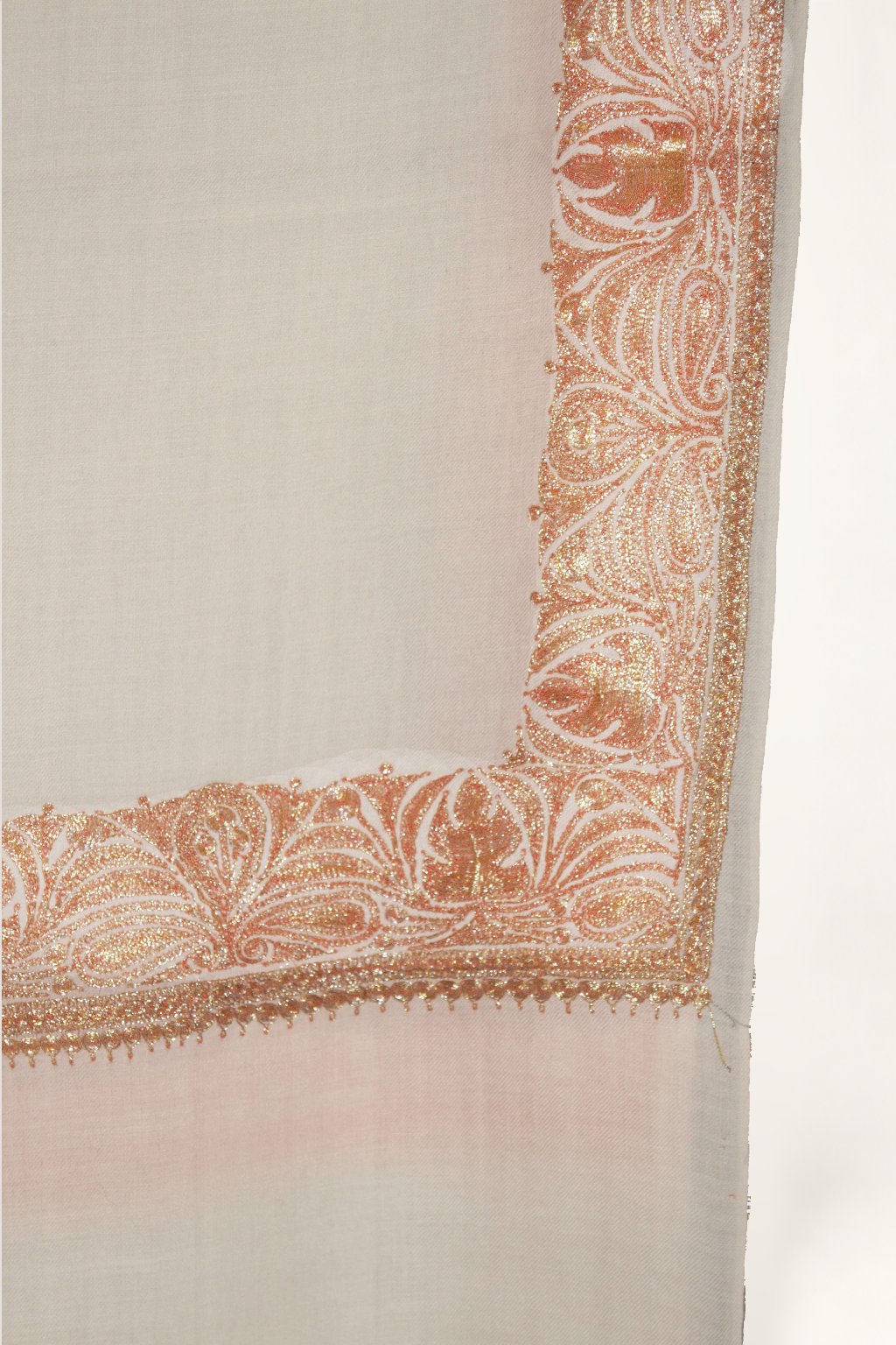 Corner close-up of ivory Merino wool shawl with peach-gold Tilla leaf embroidery along the borders and a plain end