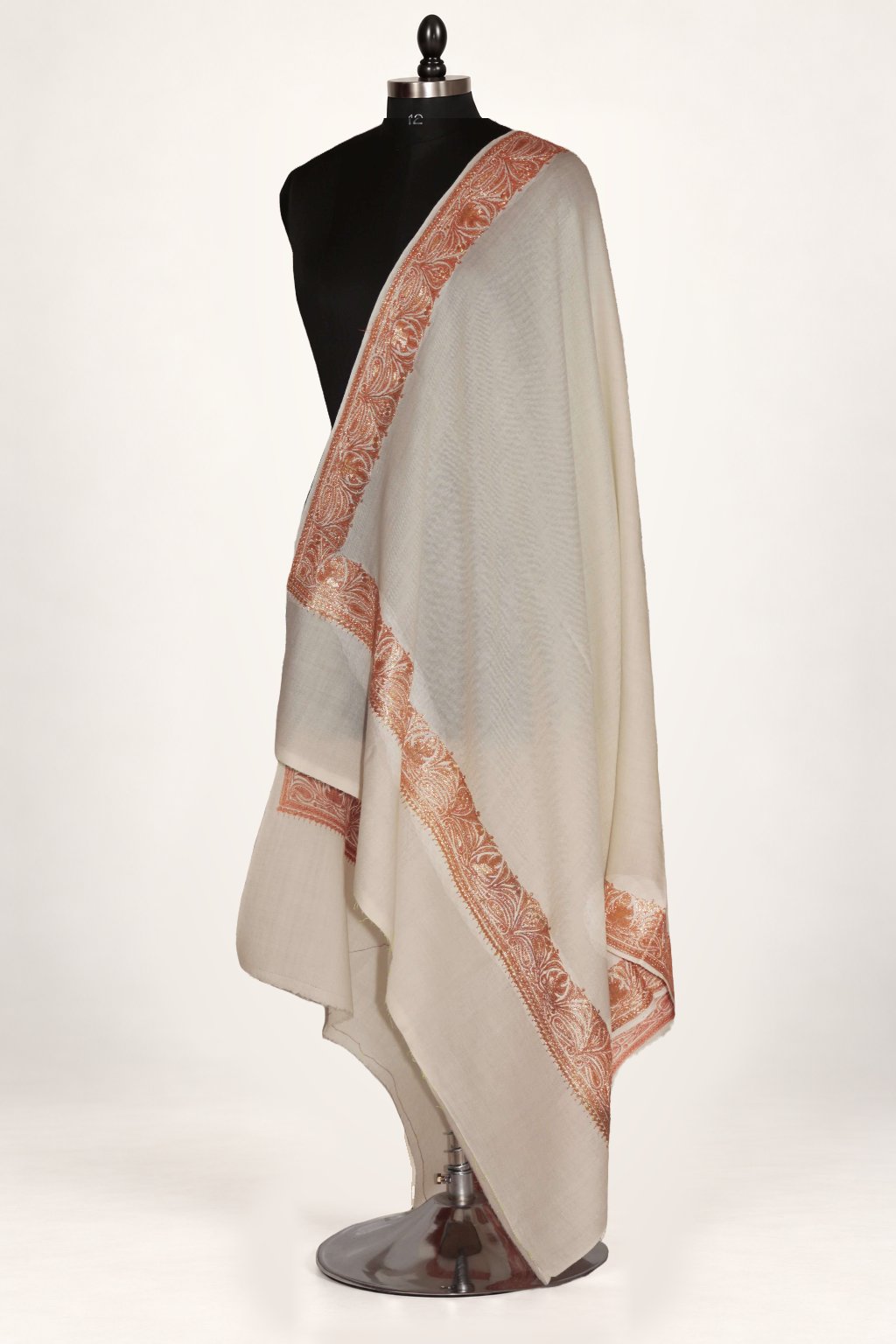 White Merino wool shawl draped on a mannequin, with peach-gold Tilla maple-leaf embroidery along its borders