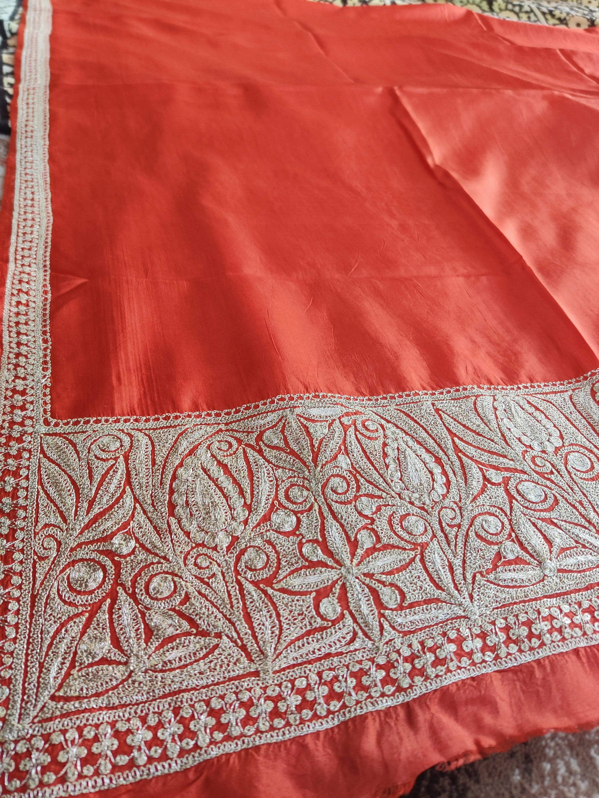 Corner detail of red silk fabric with a broad silver-toned floral Tilla border meeting a narrow embroidered side edge