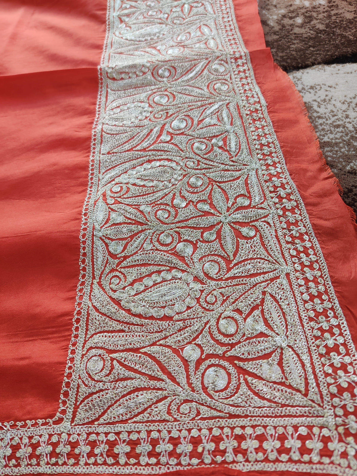 Angled close-up of silver-toned Tilla scrolling leaves and flowers along a broad red silk border