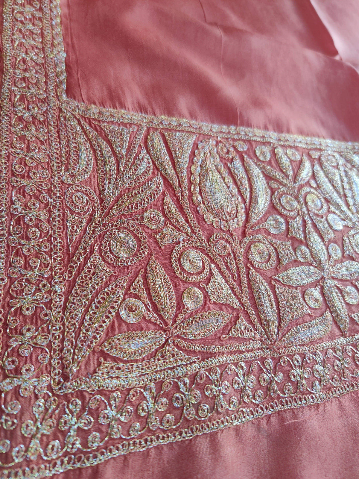 Corner detail of pale-gold flower buds, leaves and scrolling embroidery on coral-pink silk.