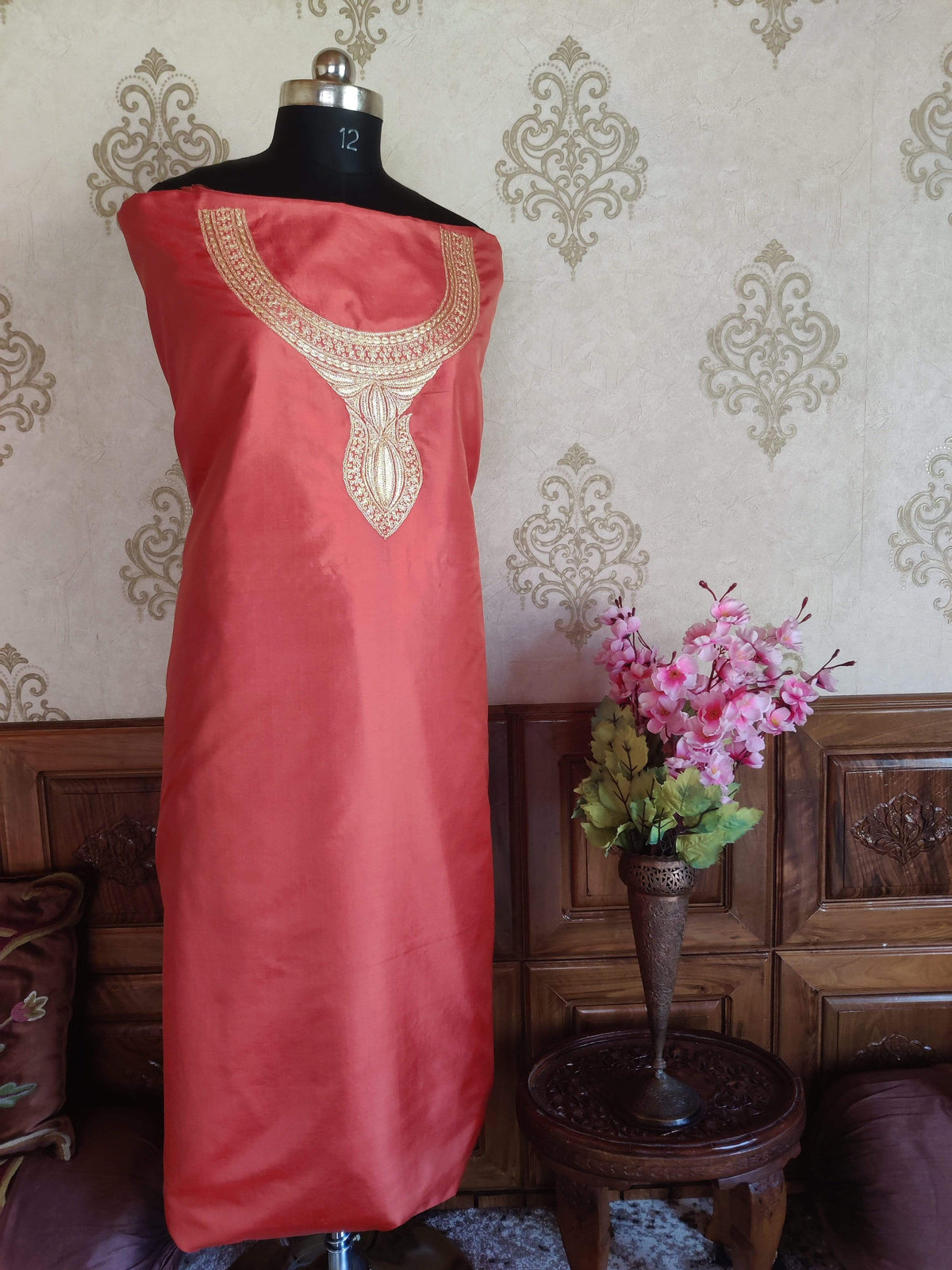 Full view of coral-pink silk suit fabric draped on a mannequin, with an ornate pale-gold neckline and plain lower section.